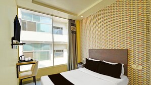 A hotel room with a bed, a desk with a chair, a TV, and a window with a view of buildings. - Classic Prayagraj Bus Stop Sonica Gold (Prayagraj)