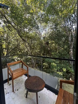 Un balcón con vistas a una vegetación densa, una mesa redonda y dos sillas de madera.