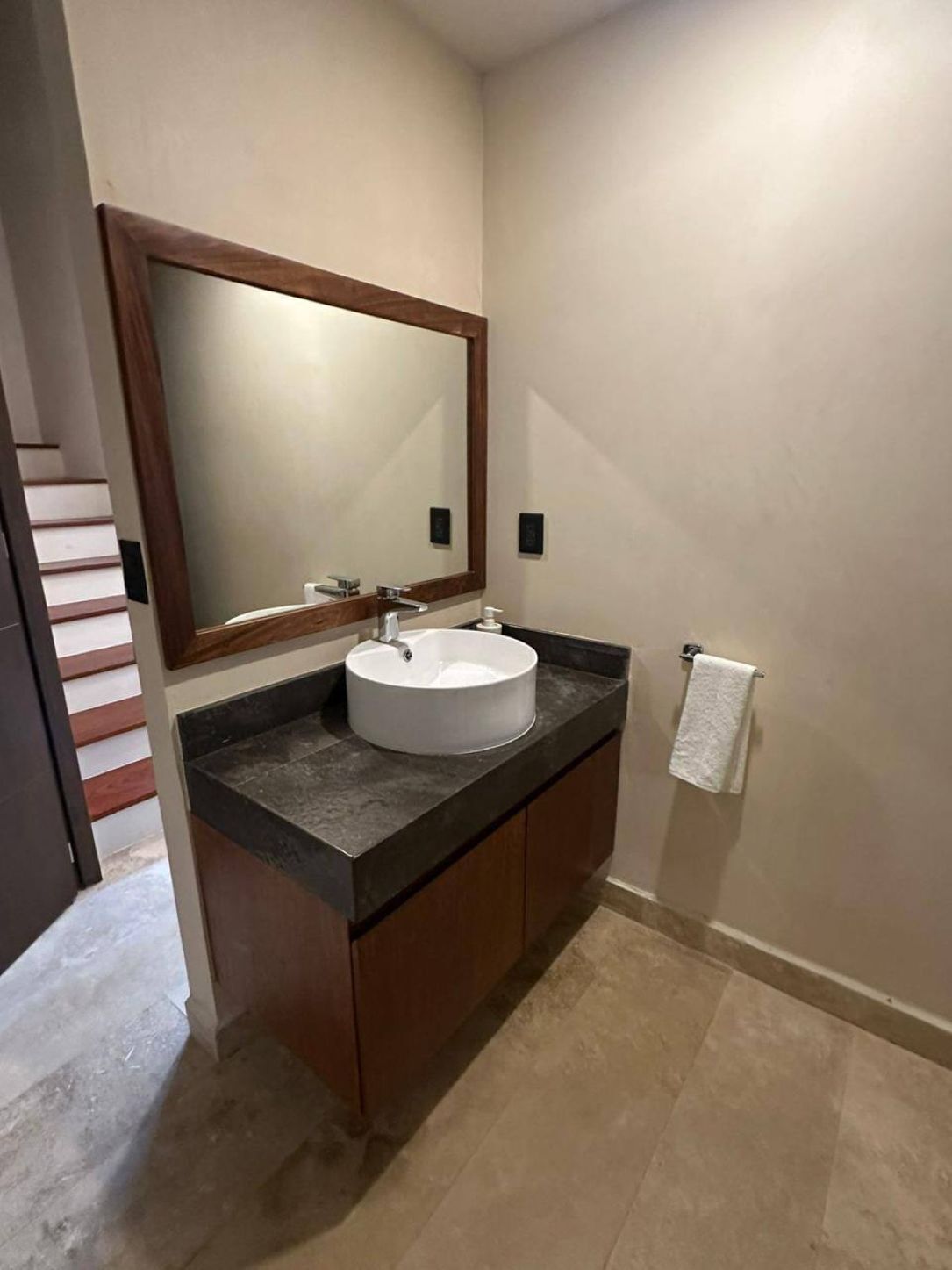 A bathroom with a white sink, dark countertop, wooden cabinets, a large mirror, and a towel hanging on the wall.
