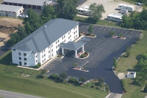 A large building with a parking lot, a covered entrance, and a small garden area.