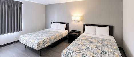 Een hotelkamer met twee eenpersoonsbedden, een nachtkastje met een lamp en een raam met gordijnen.