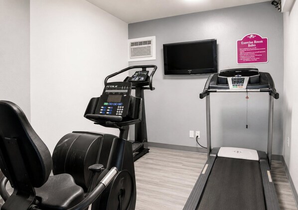A fitness room with exercise equipment, a television, and a sign with exercise room rules.