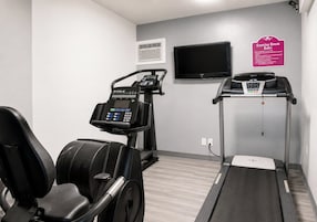 Un gimnasio con equipo de ejercicio, un televisor y un cartel con las normas del gimnasio.