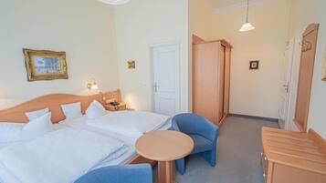 Habitación de hotel con cama doble, una mesita redonda, dos sillas azules, un armario y una lámpara.