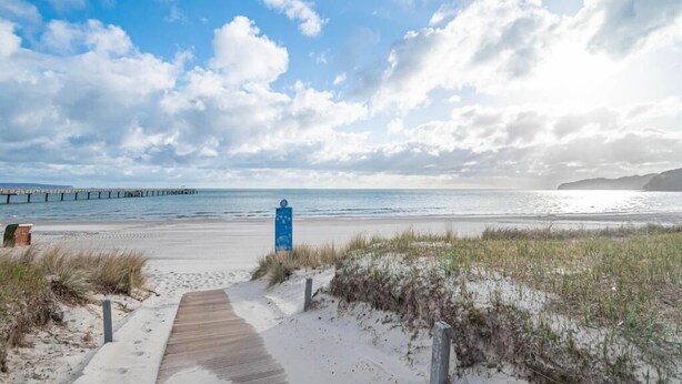 Een strandpad dat naar de zee leidt, met een pier op de achtergrond.