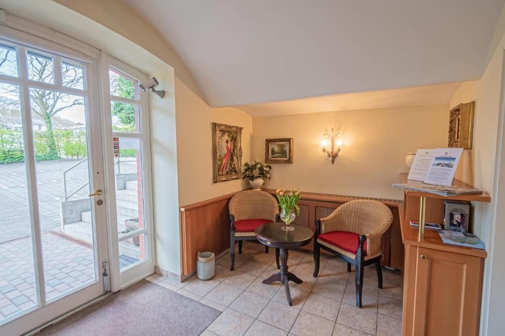 A corner room with a table, two chairs, a door leading outside, and a small cabinet with papers.