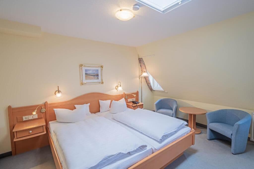 A hotel room with a large bed, bedside tables, a chair, a small table, and a picture on the wall.