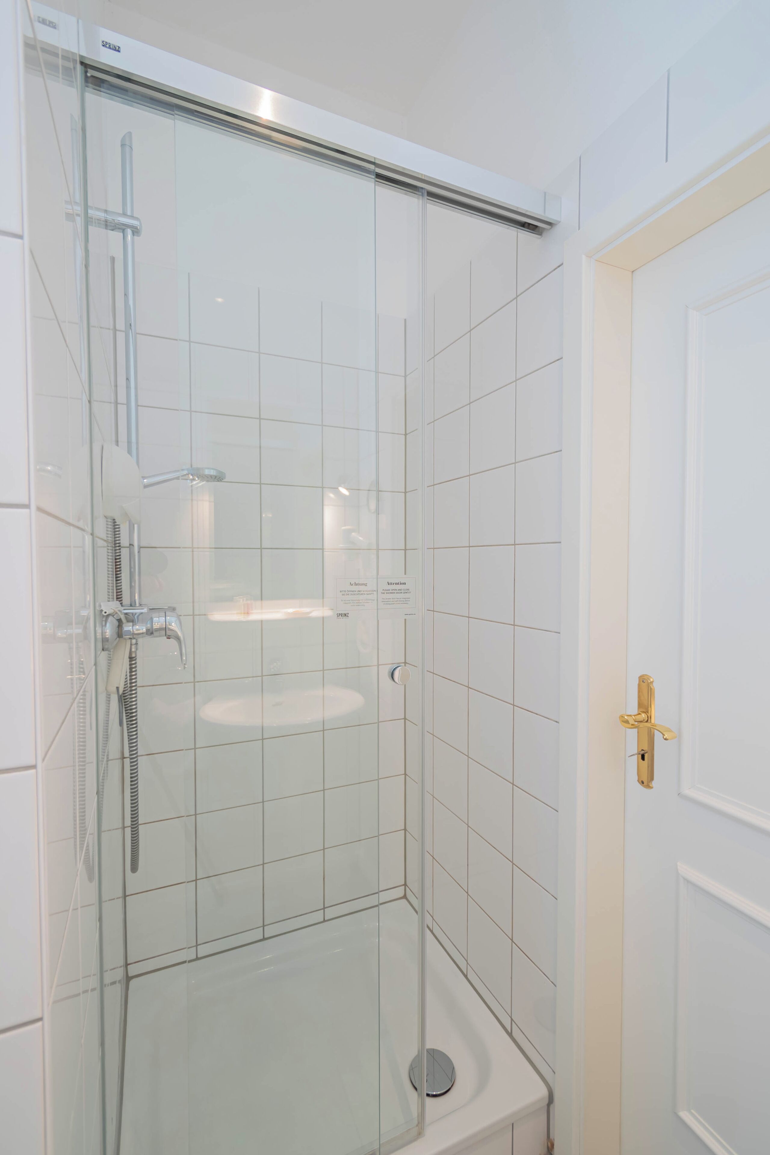 A glass-enclosed shower stall with a white sink and a door with a brass handle.