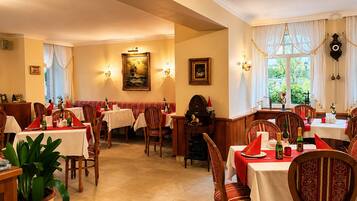A dining area with tables set for service, a clock on the wall, and a painting above the tables.