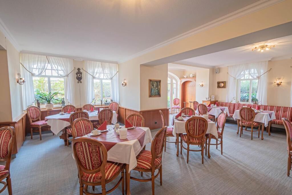 A dining area with multiple tables and chairs, large windows with curtains, and a warm interior lighting.