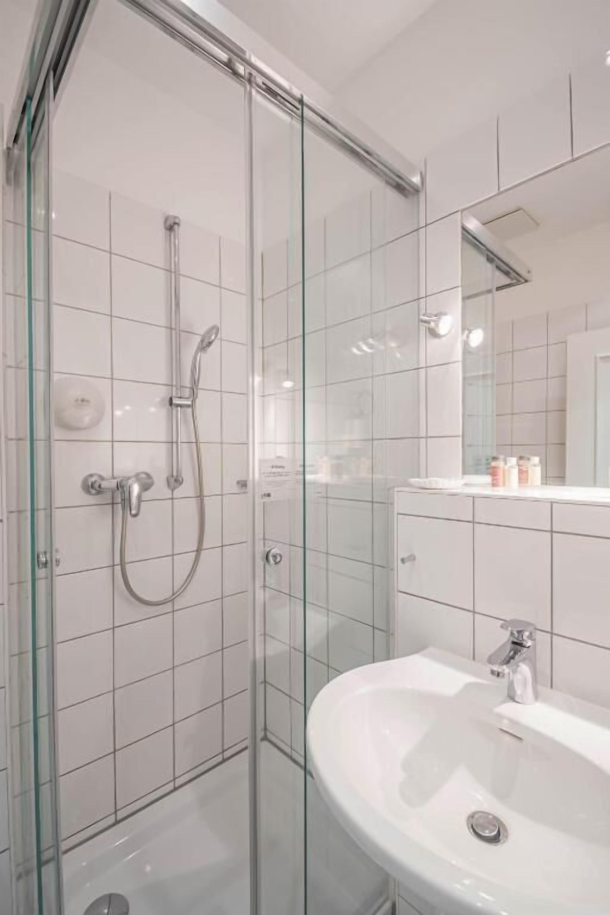 Une salle de bain moderne avec une douche à parois de verre, un lavabo blanc et un miroir au-dessus du lavabo.