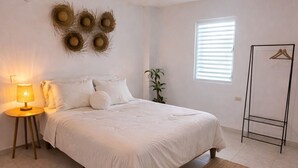 Quarto com cama, abajur, decoração na parede, janela e um suporte de metal.