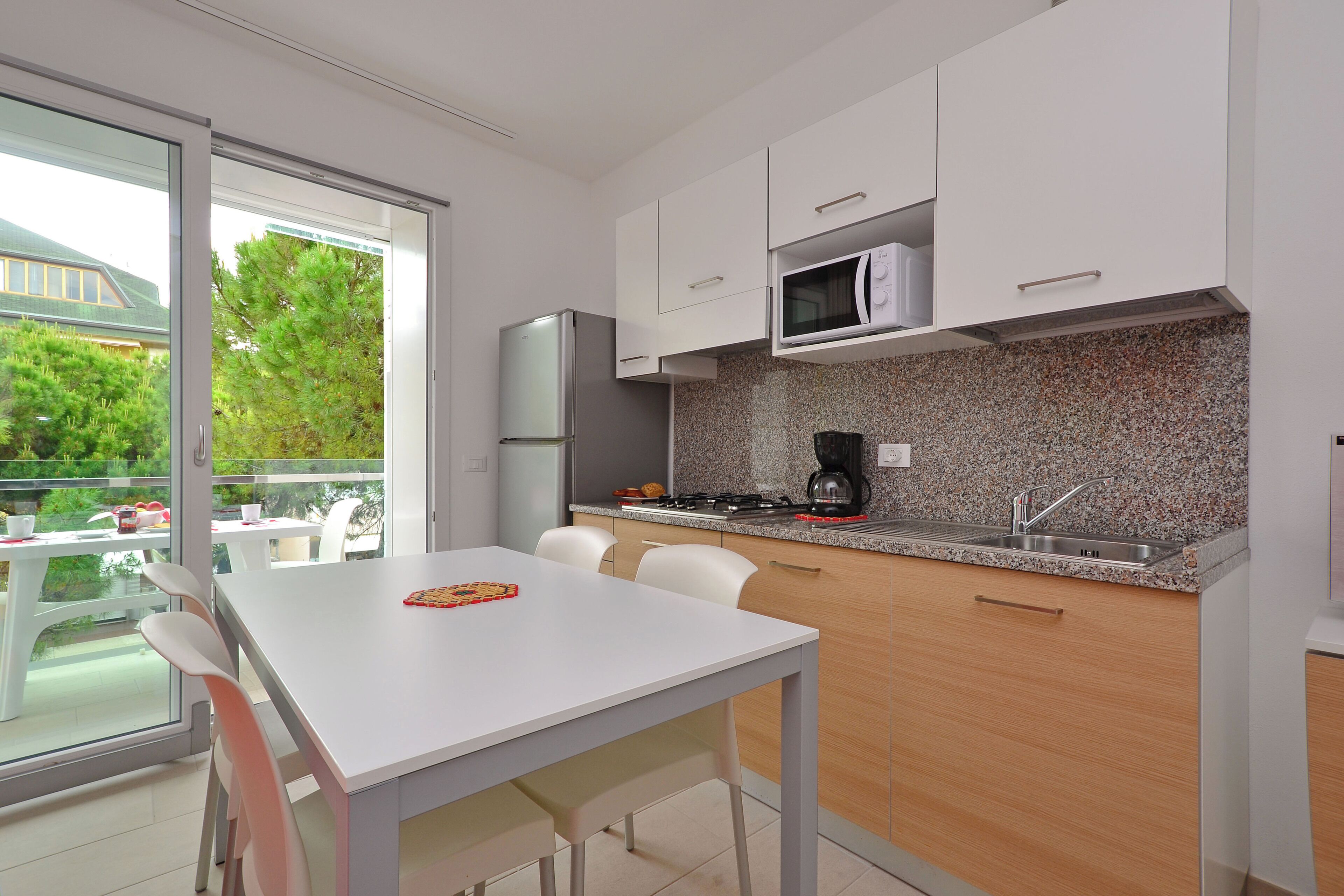 A modern kitchen with white cabinets, a granite countertop, and a large window overlooking a garden.