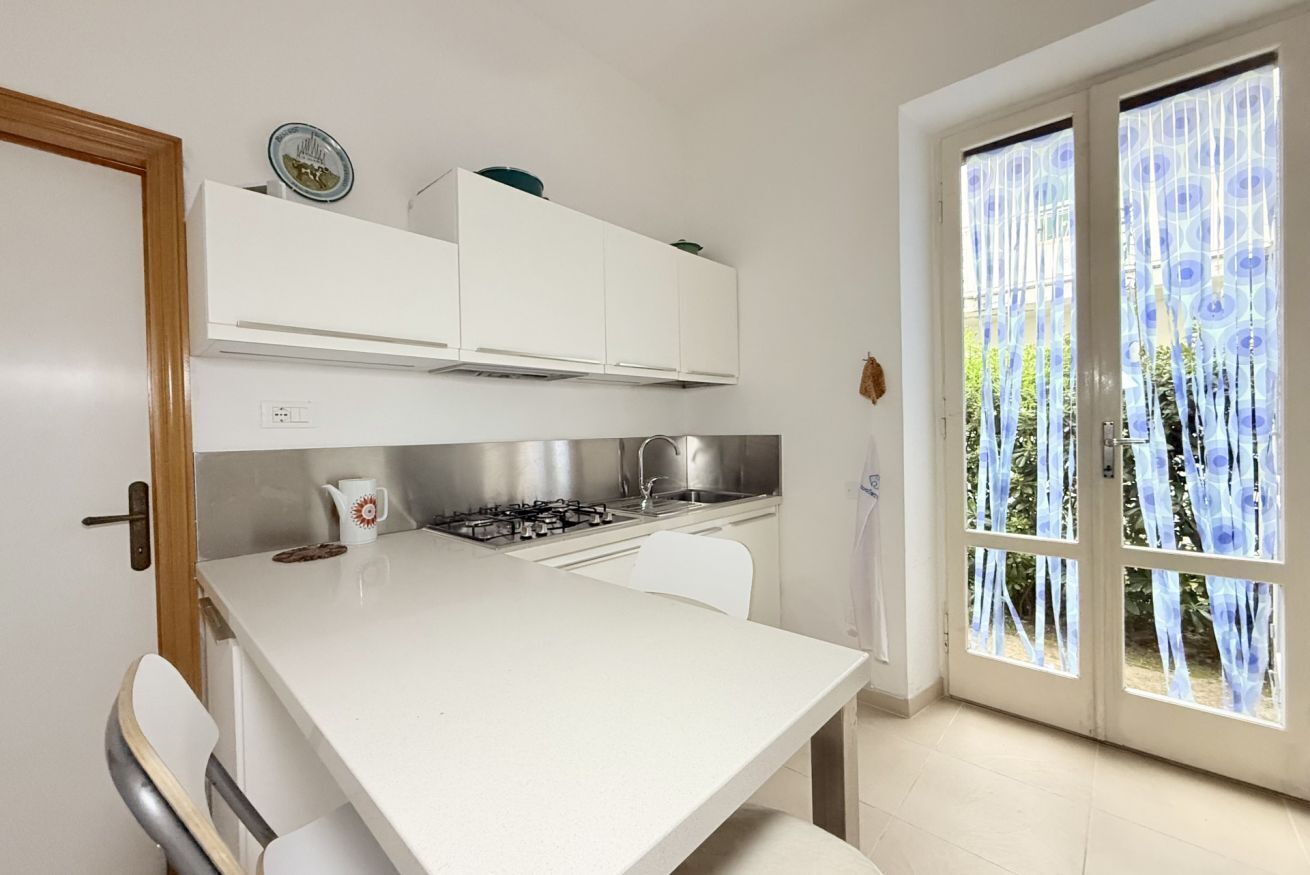 Cucina con mobili bianchi, piano cottura a gas e finestra vista verde.