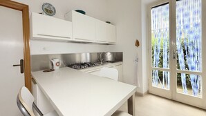 Una cocina con armarios blancos, estufa a gas y ventana con vistas al verdor.