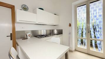 Cucina con mobili bianchi, piano cottura a gas e finestra vista verde.