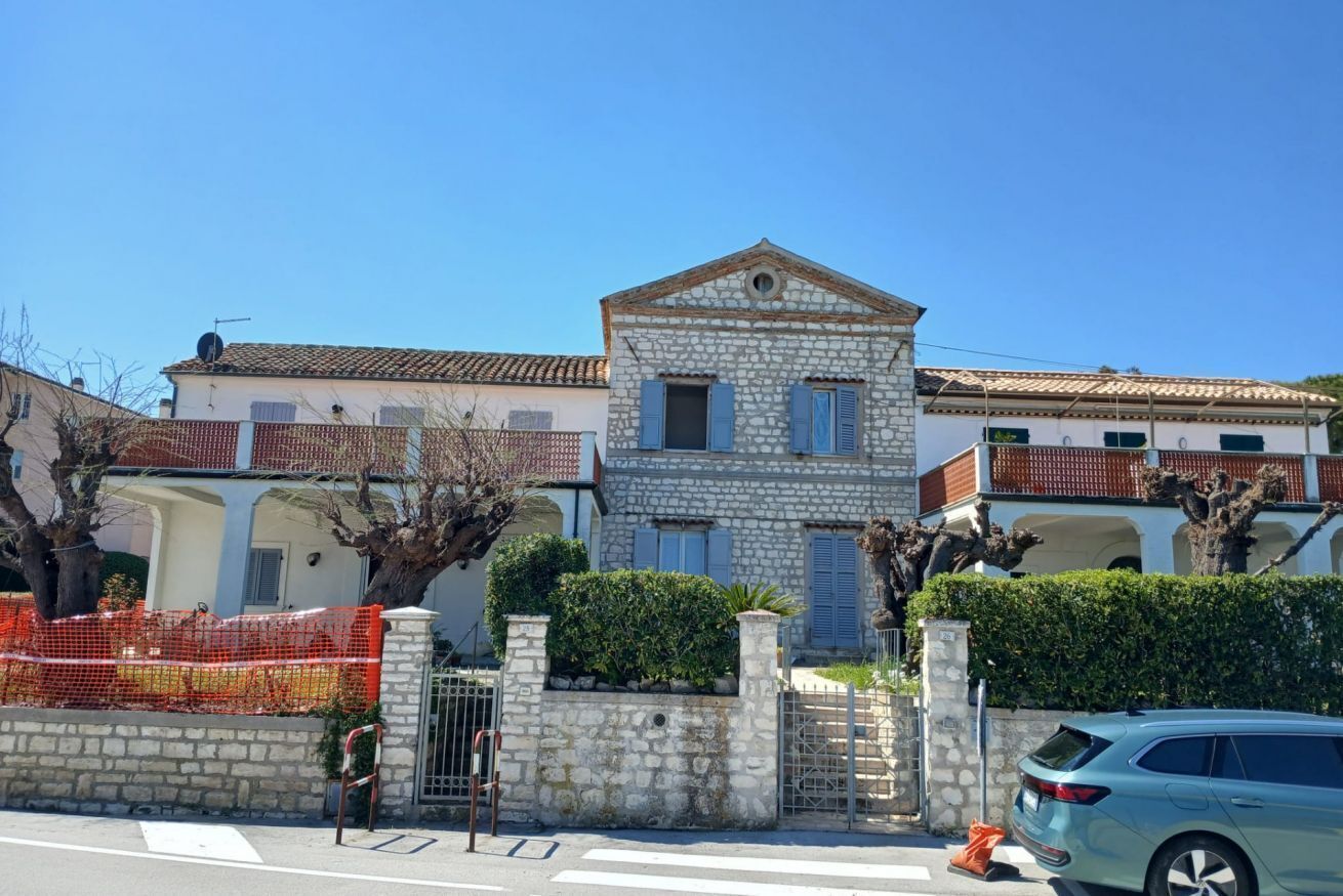 Um edifício de pedra com entrada central, varanda e um carro estacionado em frente.