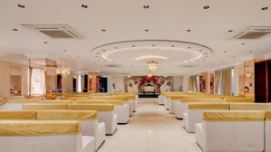 A formal room with rows of white chairs, a chandelier, and a floral arrangement at the front.