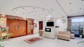 A modern lobby with a wooden door, a reception desk, a flat-screen TV, a sofa, and potted plants.