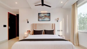 A hotel room with a large bed, a ceiling fan, a nightstand with a lamp, and a window with curtains.