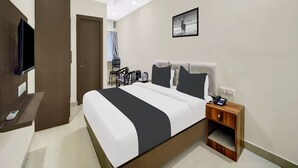 A hotel room with a bed, a desk with a chair, a television, and a picture on the wall.