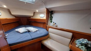 A compact cabin with a bed, a cushioned bench, a small table with a plant, and a window. - Sailing excursions in the Gulf of Naples, Boat&Bed on the port of Mergellina (Napoli)