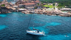 A coastal area with a sailboat anchored near rocky terrain and buildings. - Sailing excursions in the Gulf of Naples, Boat&Bed on the port of Mergellina (Napoli)
