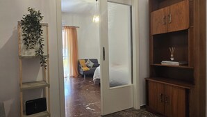 A room with a marble floor, a wooden bookshelf, a framed plant, and a door leading to another room. - Central Athens Home | 2BR, Near Metro Green & Red Line & Uni, Bills included (Athina)