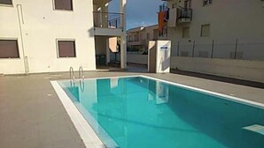 Una piscina con escalones de acceso, rodeada por un edificio con balcones y ventanas.