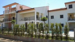 Un edificio residencial de varios pisos con balcones, piscina y jardín cercado.