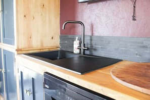 A kitchen with a black sink, wooden cabinets, a dishwasher, and a pink wall.