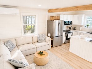 A modern kitchen with white cabinets, a stainless steel refrigerator, and a wooden dining table. - “Waterfront cabin w/ private deck overlooking the ocean & amazing sunset views.” (Cushing)