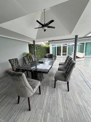 A covered outdoor dining area with a marble table and tufted chairs, a ceiling fan, and a view of the outside. - 5 Bedrooms Villa 5 min Walk to Bangtao Beach (Si Sunthon)