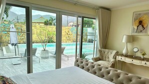 Habitación de hotel con cama, sofá, escritorio, silla y vistas a una piscina y montañas.