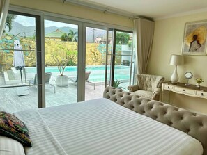 Ein Hotelzimmer mit Bett, einer Couch, einem Schreibtisch, einem Stuhl und Blick auf einen Swimmingpool und Berge.