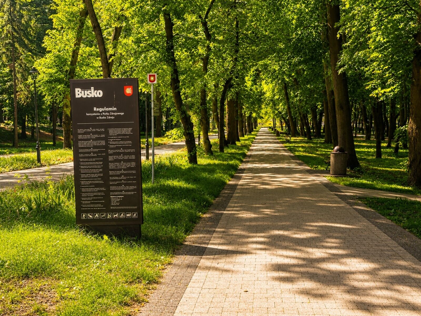 A paved pathway lined with trees, a signboard with text, and a red stop sign.