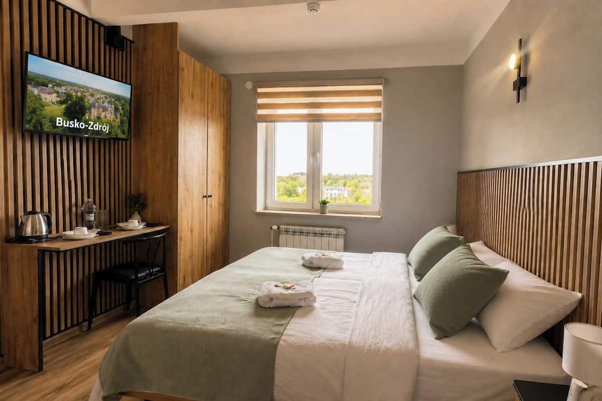 Una camera d'albergo con un letto, una scrivania con un bollitore, una televisione e una finestra con persiane.