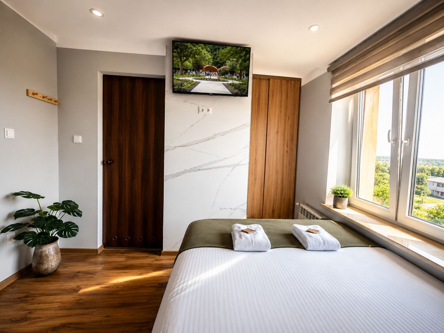 A modern bedroom with a large bed, wooden door, marble wall, and a TV mounted above the bed.