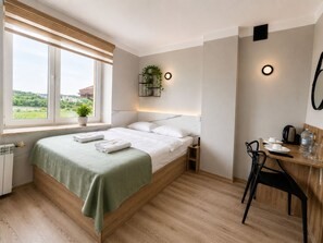 A bedroom with a bed, a bedside table, a chair, a desk, a potted plant, and a window with a view.