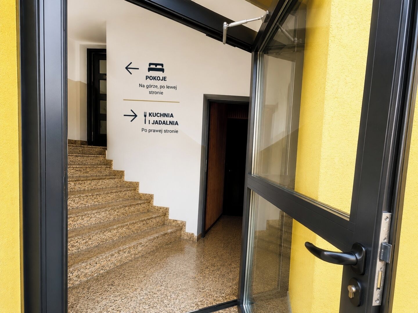 Escada que leva a um ambiente com sinalização indicando o caminho para a cozinha e a sala de jantar.