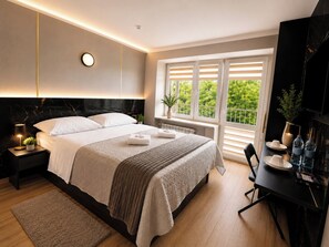A modern bedroom with a large bed, bedside tables, a desk, and a window with blinds.