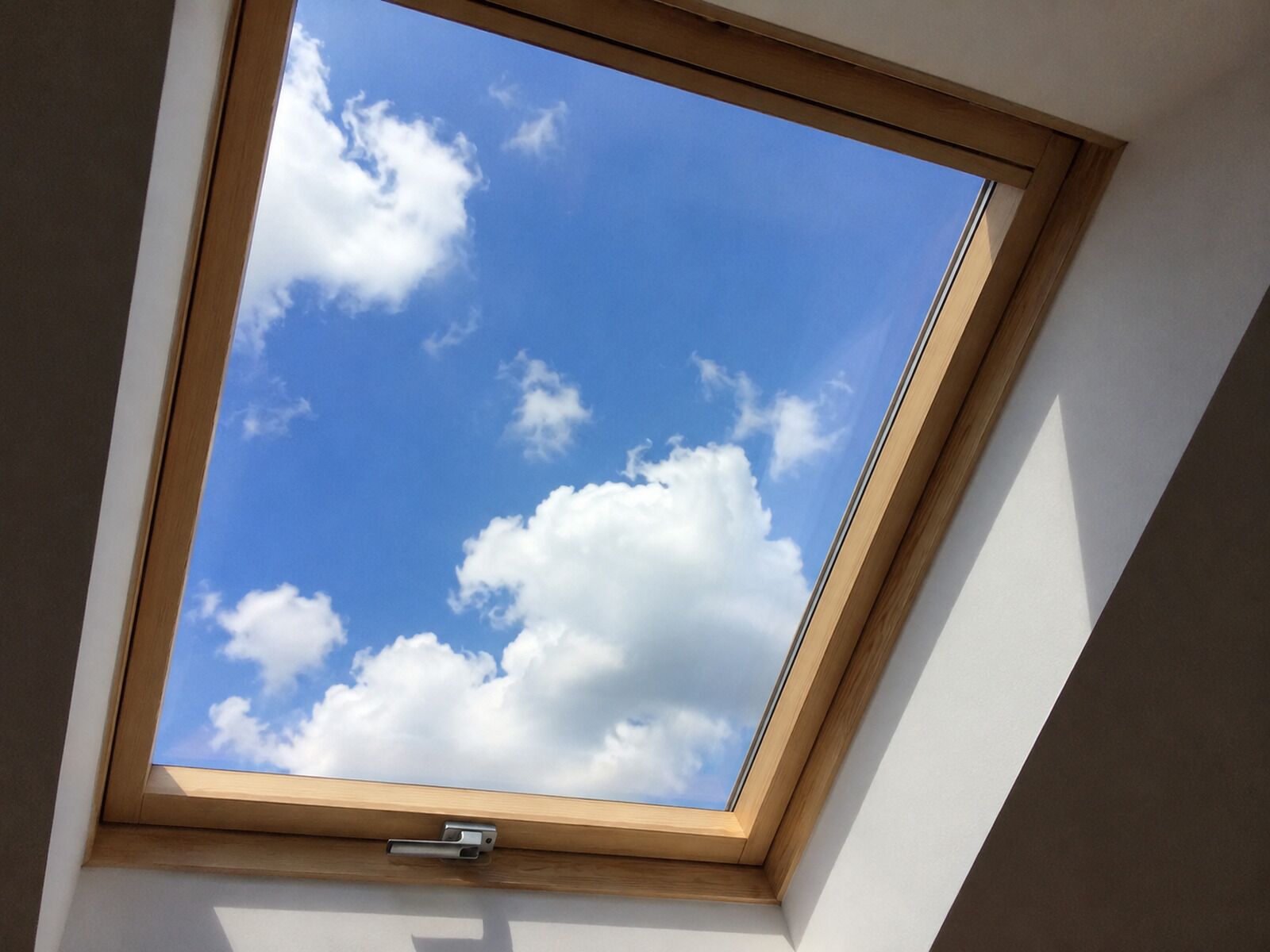 Une lucarne laissant apparaître un ciel bleu azur et des nuages.