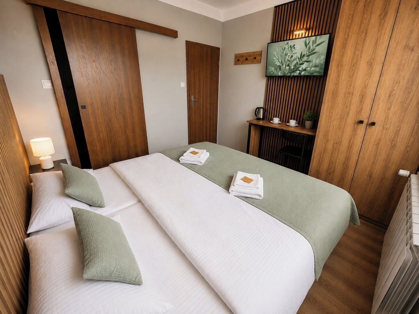 Ein Hotelzimmer mit zwei Betten, einem Holzschrank, einem Fernseher und einem kleinen Tisch mit einer Pflanze.