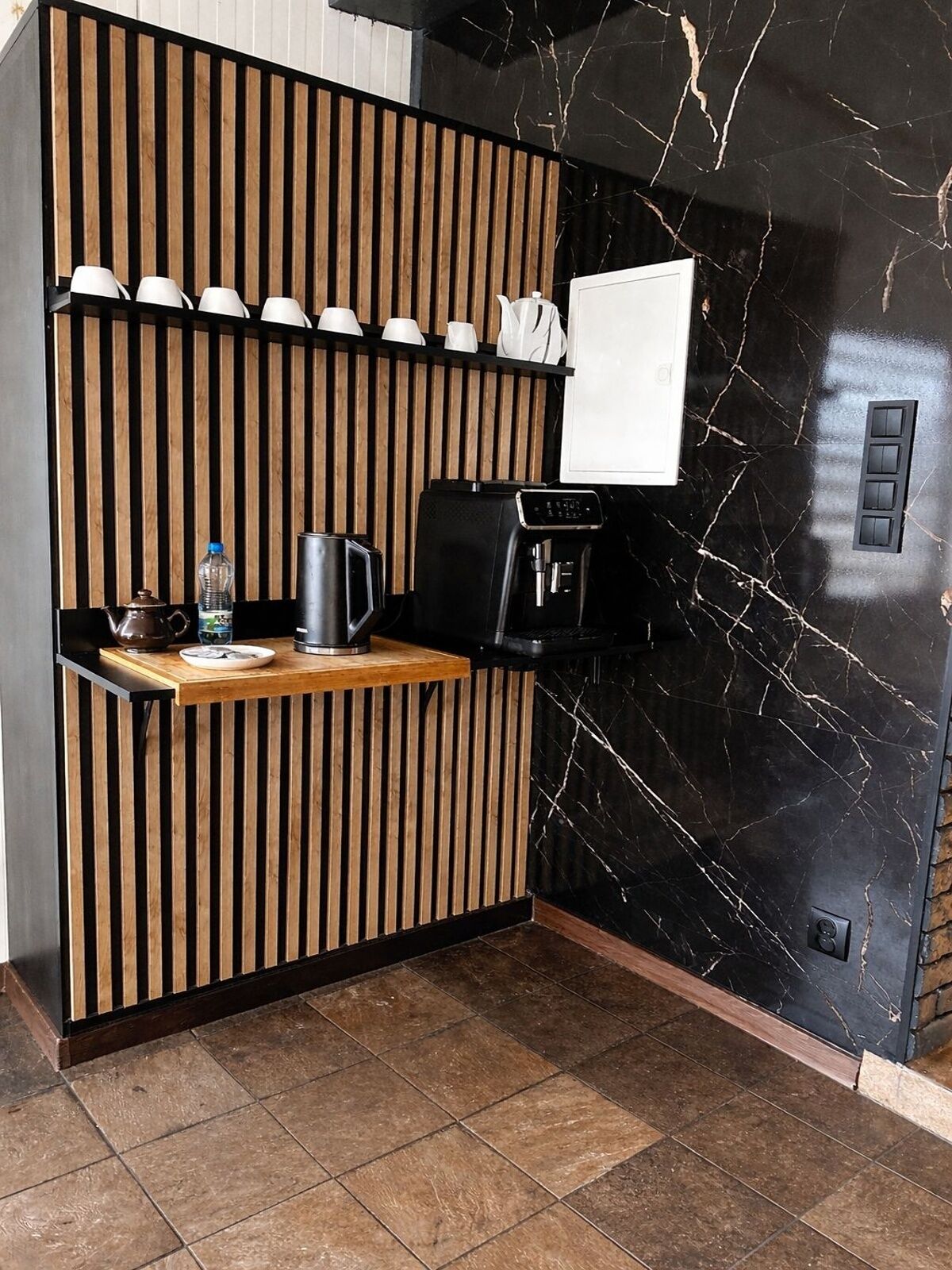 A compact kitchenette with a coffee machine, a kettle, and a water bottle on a wooden counter.