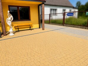 A yellow building with a bench and a statue, a 'Parking' sign, and a paved walkway.