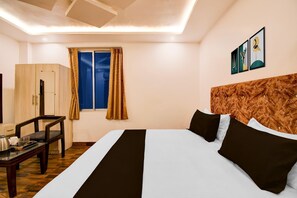 Habitación de hotel con cama, escritorio, silla, armario y ventana con cortinas.