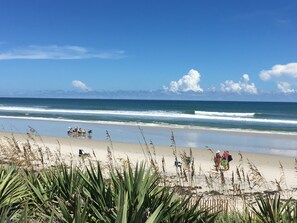 A beach with people sitting and walking along the shore, and waves crashing onto the sand. - Cozy 2-bedroom condo in tranquil New Smyrna Beach with breathtaking views (New Smyrna Beach)