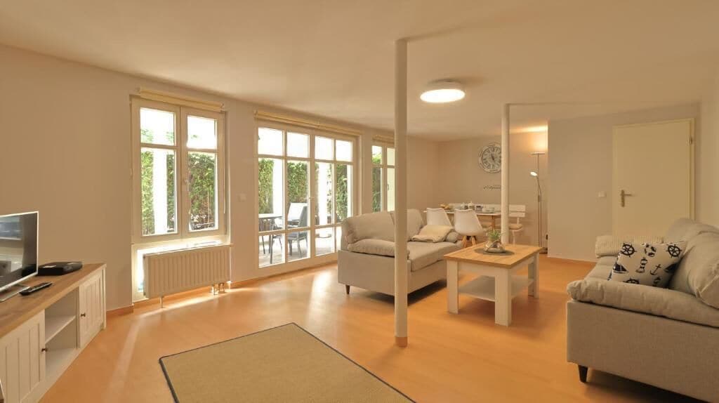 Amplia sala de estar con sofá, mesa de centro y televisor. Grandes ventanas permiten luz natural y vistas al exterior.