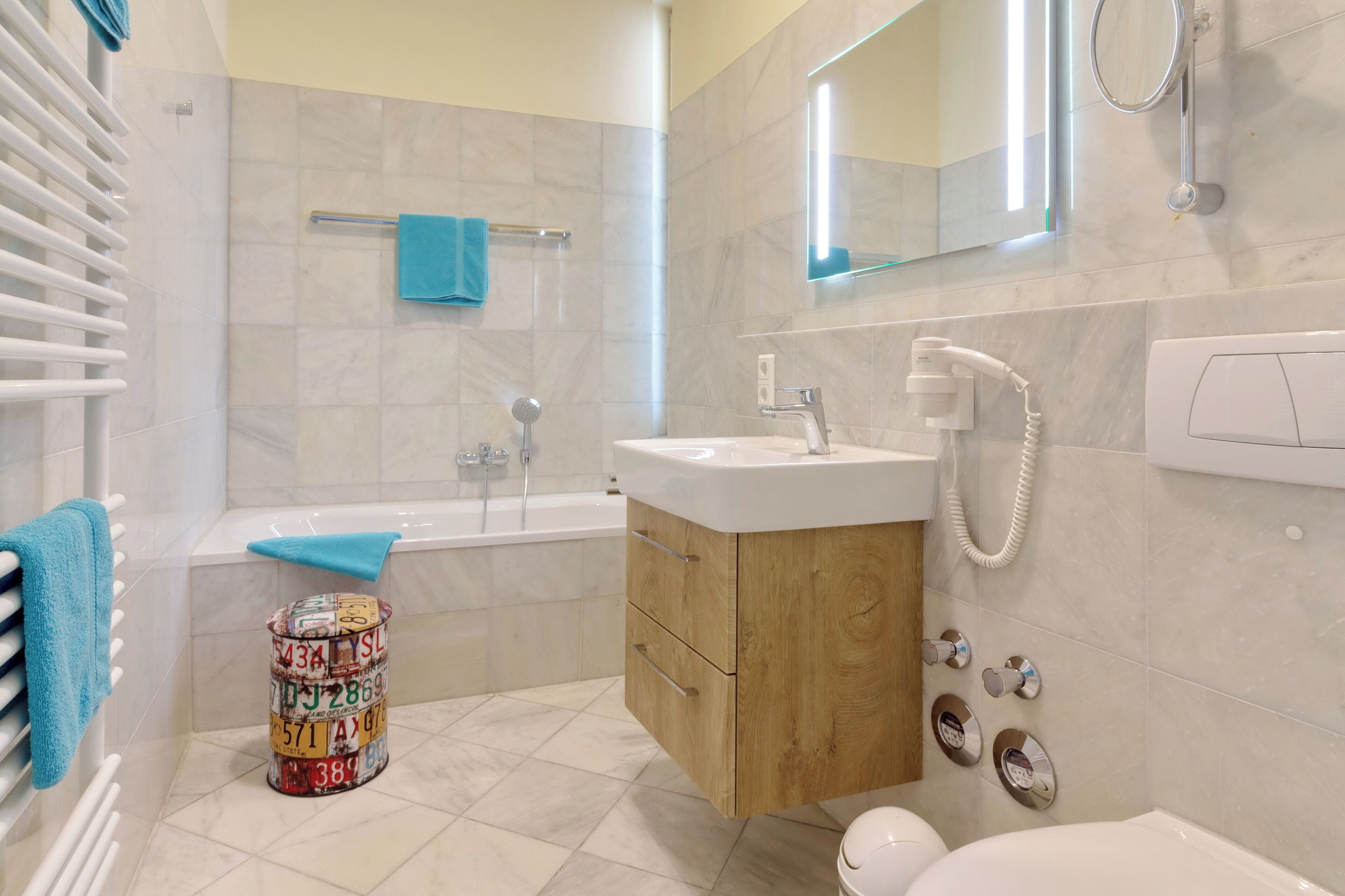 Et moderne badeværelse med badekar, håndvask med håndbruser, toilet og trækommode.
