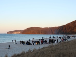 A beach with people gathered, a sandy shore, and a forested hill in the background.